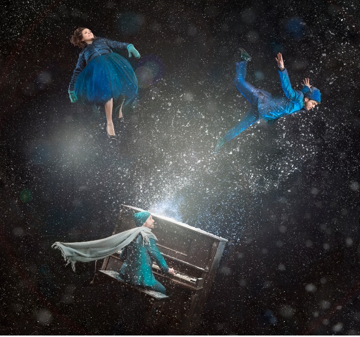 Three people floating in the air dressed in blue with one man playing a piano. 