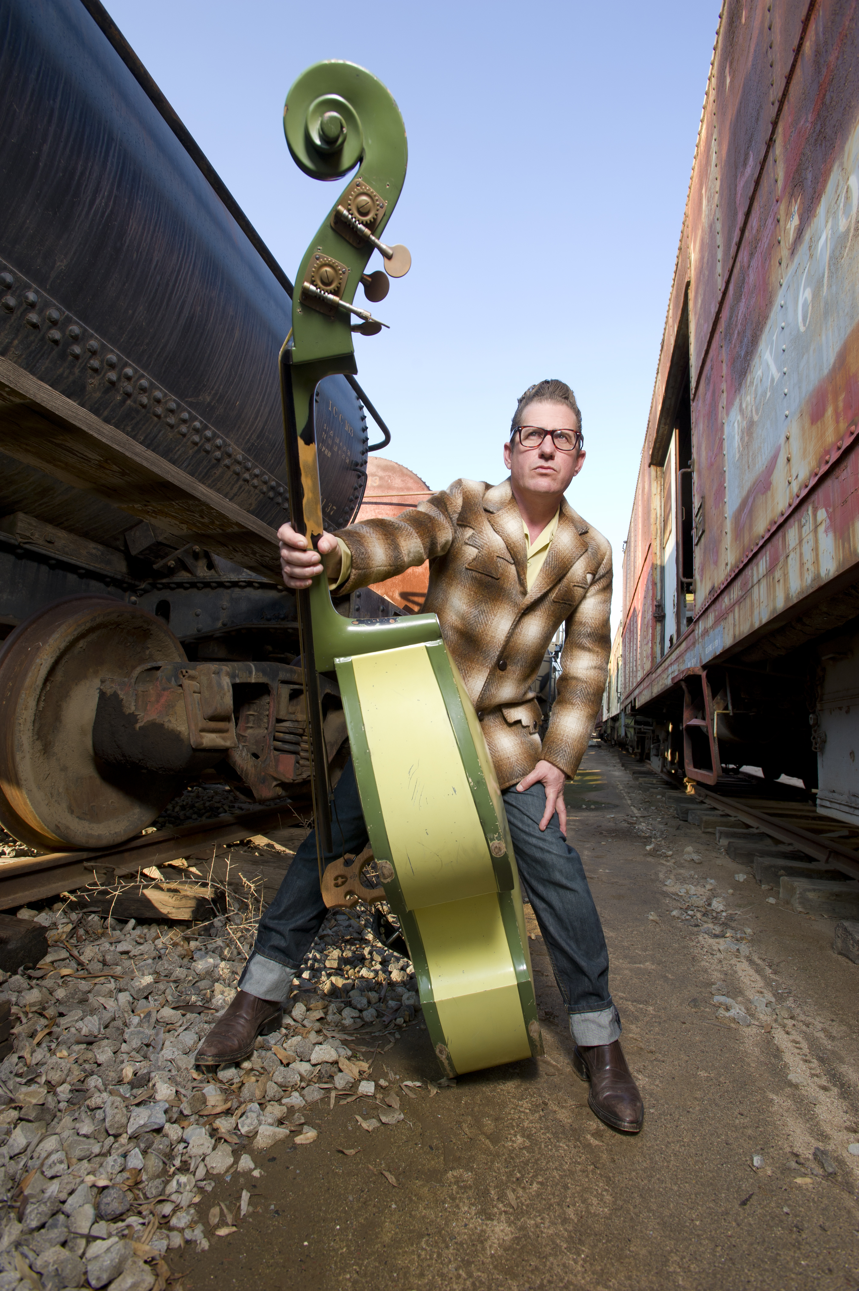 Lee Rocker in between two trains with his bass guitar.