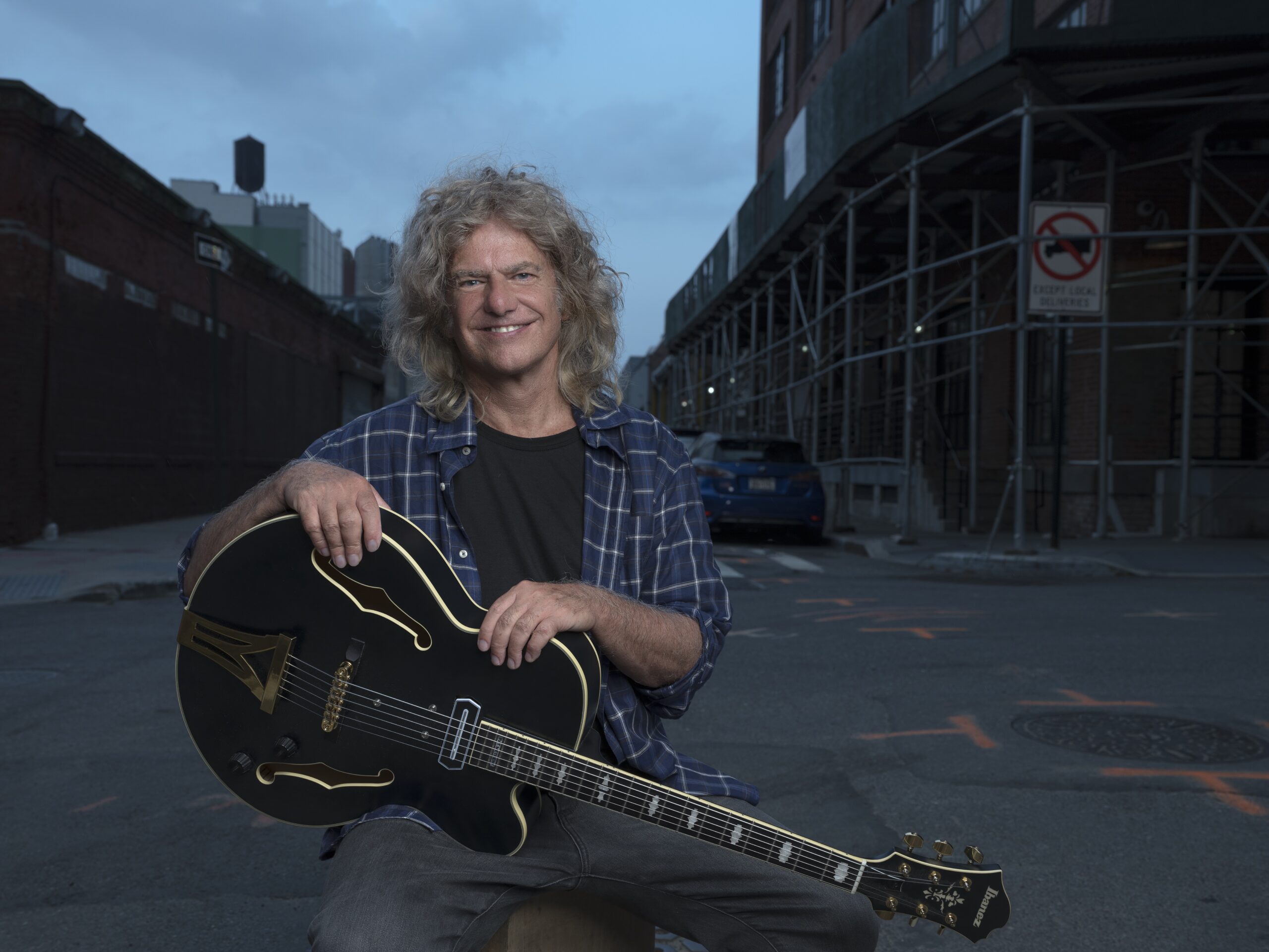 Pat Metheny in street landscape holding a guitar.