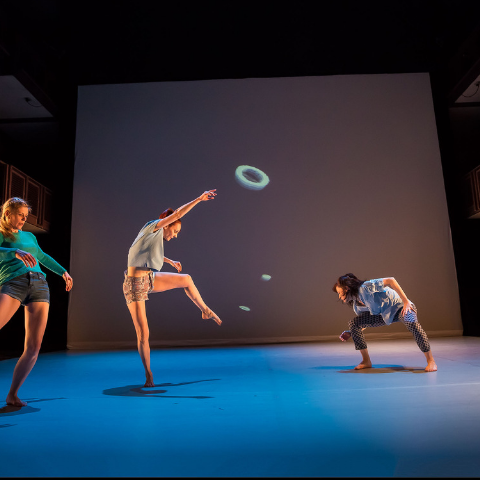 Dancers on stage in front of a drop down digital screen. 