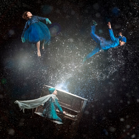 Three people floating in the air dressed in blue with one man playing a piano. 