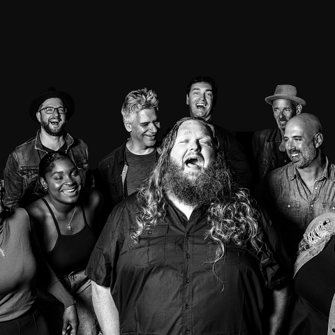 Matt Andersen, a white, long haired gentleman, singing with his head thrown back and his accompanying group surrounding him.