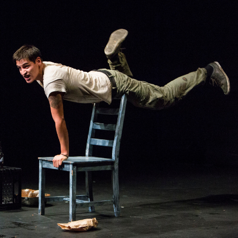 Man holding himself up off the back of a chair.