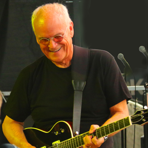 A smiling Ian Thomas with guitar on stage