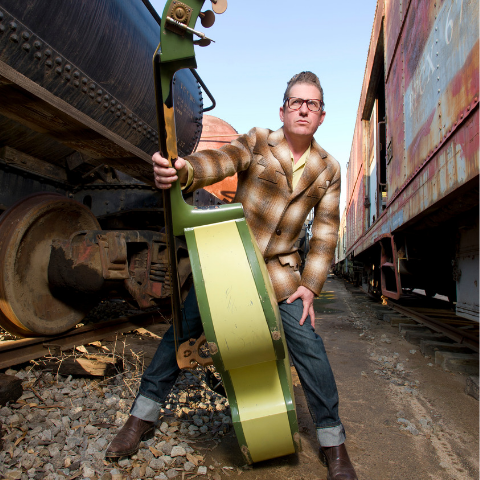 Lee Rocker in between two trains with his bass guitar.