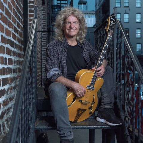 Pat Metheny with guitar on fire escape stairs in urban environment