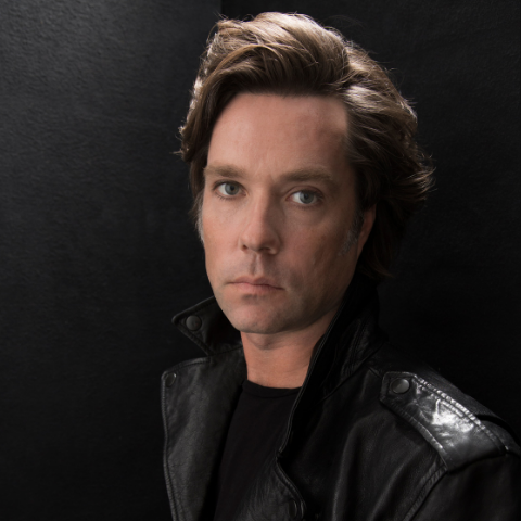 Rufus Wainwright posing in a black leather jacket.