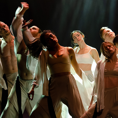 multiple dancers on stage, some with their arms in the air