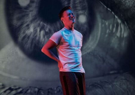 A man wearing a white t-shirt standing in front of a projected image of an eye