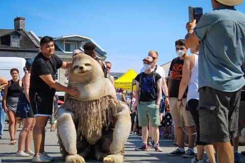 A man performing outside with a life size puppet of a giant sloth