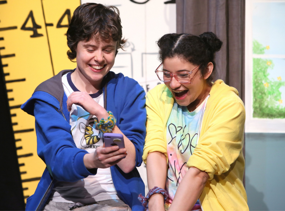 Two young female actors looking at a cell phone and laughing.