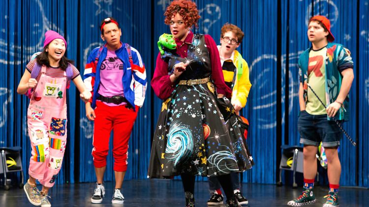 Photo of performers wearing bright and colourful clothing standing on a stage.