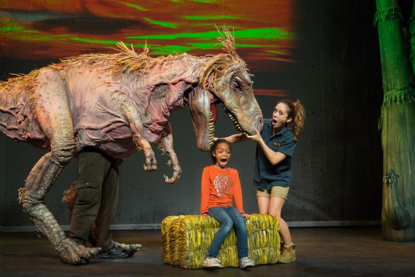 small child on stage with a large dinosaur puppet over them