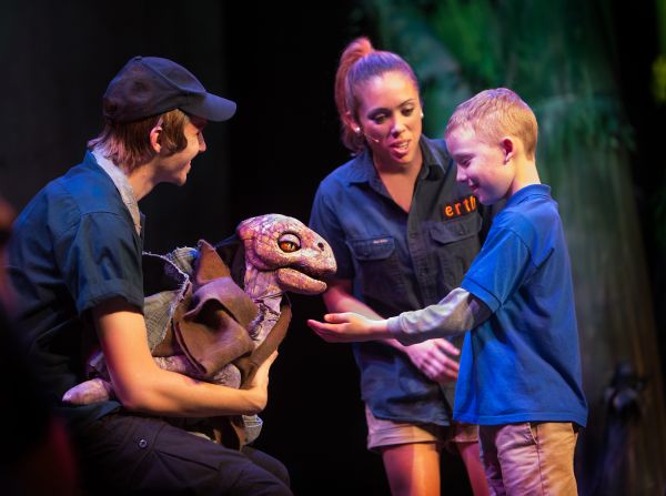 child petting a baby dinosaur on stage