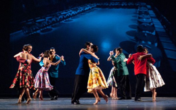 brightly dressed tango dancers, in a line on a dark stage