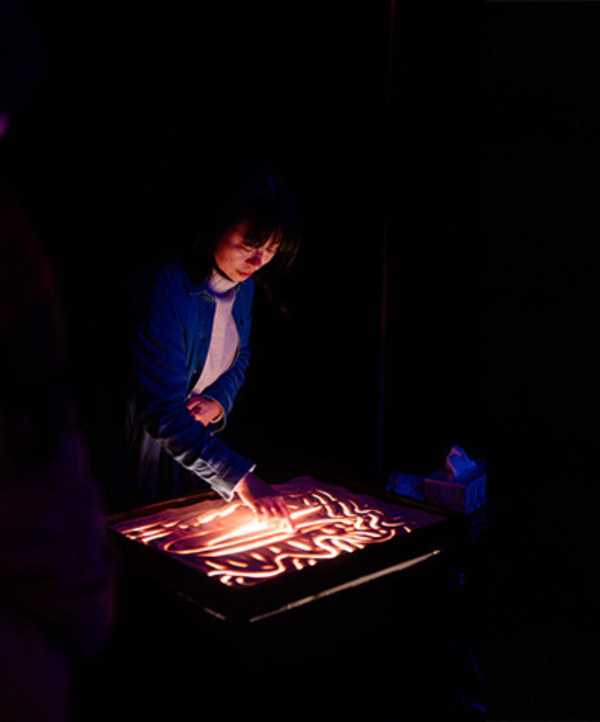 a lady leaning over a back lit table with finger painting on top